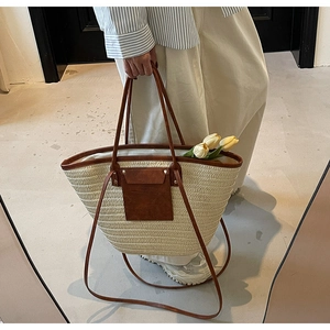 Detail view of woven straw tote bag featuring brown leather handles and rivet accents