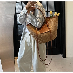 Detail of a large straw tote bag featuring brown leather straps and a front pocket design