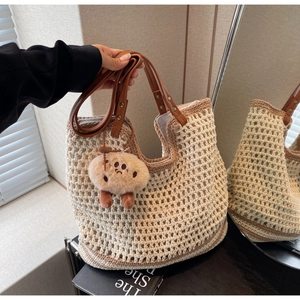 Detail of woven bucket bag with brown leather handles and plush cookie charm