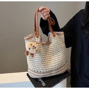 Detail of beige woven bucket bag with leather handles and a plush doll accessory