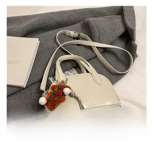 Detail view of cream bowling bag with plush bear charm on a wool coat background