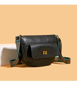 Détail du sac besace en cuir noir avec large bandoulière brodée et boucle dorée élégante