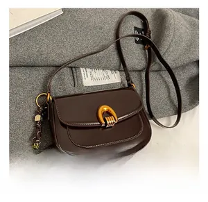 Detail of dark brown leather saddle bag featuring a golden horseshoe buckle and bear charm