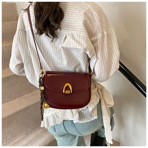 Detail of burgundy leather saddle bag with gold U-shaped buckle and woven charm