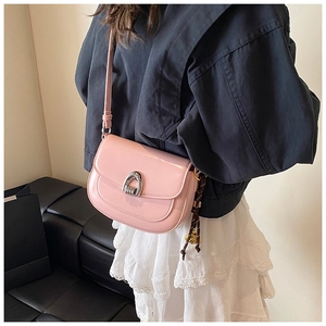 Pink patent leather saddle bag worn cross-body with silver buckle and woven pendant detail