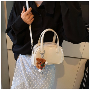 Close-up of a cream white Boston bag featuring a cute plush bear charm and smooth finish