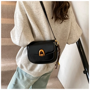 Detailed view of black faux leather saddle bag with gold U-shaped buckle and woven charm