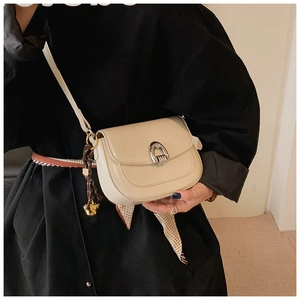 Detail of a beige saddle bag featuring a silver horseshoe buckle and dark brown charm