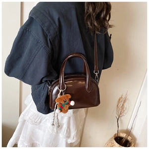 Detail of deep brown glossy bowling bag with cute plush bear charm on a model's shoulder