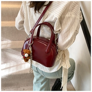 Close-up of burgundy bowling bag with a teddy bear charm on a striped shirt outfit