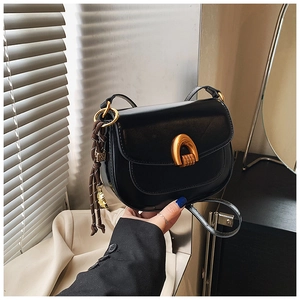 Detail of black leather saddle bag with gold metal buckle and woven tassel charm