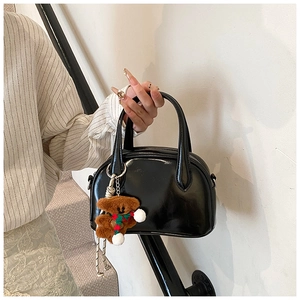 Detail of black glossy leather bowling bag with a cute brown plush bear charm