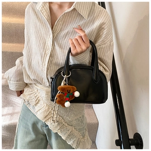 Detail of black bowling handbag with a cute brown plush bear charm and dual handles