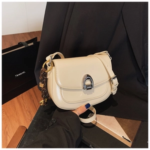 Detail view of cream saddle bag featuring a U-shaped silver buckle and woven charm pendant