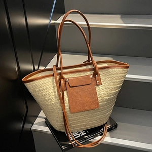 Straw tote bag with brown leather trim and shoulder strap on grey urban stairs
