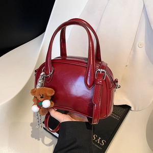 Retro burgundy bowling bag with bear charm shown in a professional handheld style