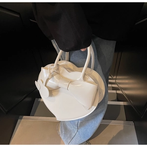 Détail d'un sac à main blanc en forme de cœur avec un grand nœud tenu à la main