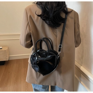 Gros plan d'un sac à main noir en forme de cœur avec nœud et breloque sur un modèle