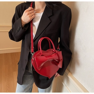 Sac à main rouge en forme de cœur avec grand nœud porté par un mannequin en blazer