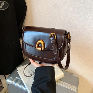 Dark brown leather saddle bag with gold U-shaped buckle, styled as a shoulder crossbody bag