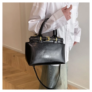 Dettaglio di una borsa tote in pelle nera lucida con fibbia dorata tenuta da una modella