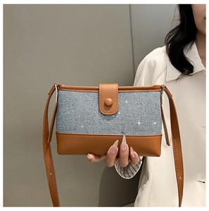 Detail of light blue denim and brown leather stitching on a small square shoulder bag