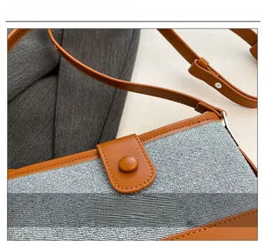 Detail view of grey canvas shoulder bag with brown leather trim and metallic buckle