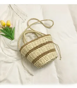 Détail du sac seau en paille tissée à rayures avec cordon de serrage sur tissu blanc