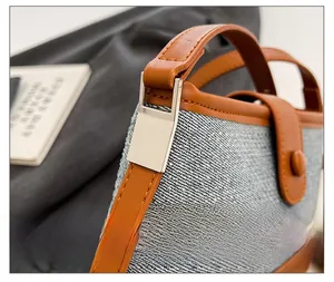 Macro view of silver metal buckles and brown leather trim on a blue denim shoulder bag