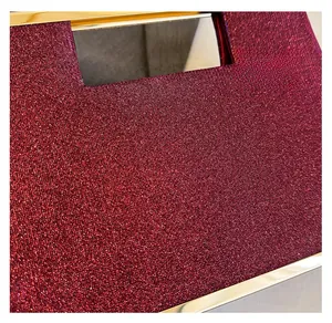 Dettaglio del tessuto a paillettes rosso vino e del manico in metallo dorato della borsa