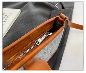 Detail of silver metal zipper with engraved logo and brown leather trim on a textured bag