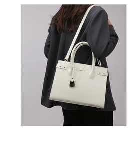 Rear view of a model carrying a white tote bag with light gold charms on a grey suit