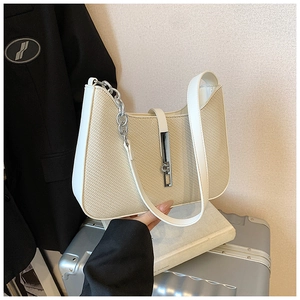 Détail du sac beige tressé avec bordure en cuir blanc sur une valise argentée
