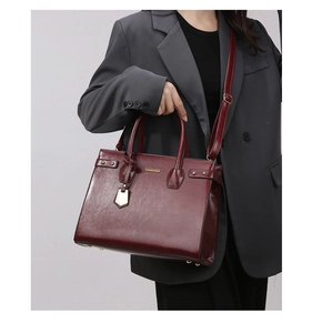 Detail of burgundy synthetic leather tote bag with metallic studs and logo plate on model