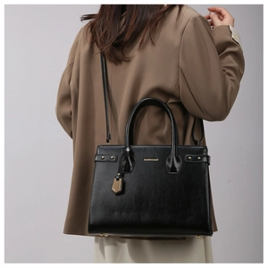 Detail of black glossy tote bag with gold lettering shown from a side view on a model