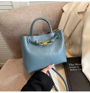 Detail of blue faux crocodile texture bag with gold hardware on a beige chair