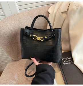 Detail of crocodile pattern handbag with gold knot hardware and woven shoulder strap