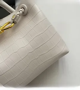 Detailed close-up of cream crocodile pattern handbag with gold hardware and woven handle