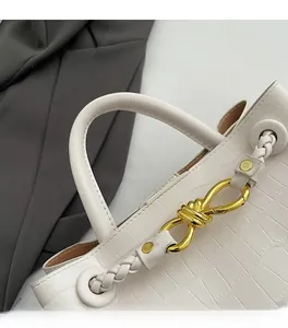 Detailed macro view of cream crocodile-embossed leather bag with gold knot buckle