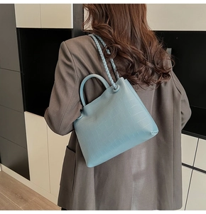 Light blue croc-embossed tote bag shown on model in a minimalist indoor setting