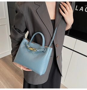 Close-up of light blue crocodile texture handbag with woven handle and gold knot buckle
