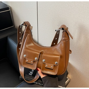 Detail of brown leather crescent bag featuring silver rivets and two utility flap pockets
