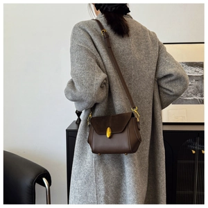 Side view of a vintage brown leather crossbody bag with gold buckle on a wool coat