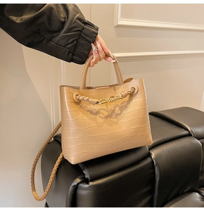 Detail of beige crocodile pattern handbag with golden twist clasp and woven strap