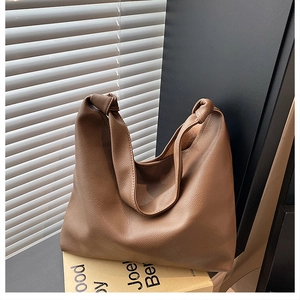 Detailed close-up of brown textured leather tote bag featuring a decorative knotted strap