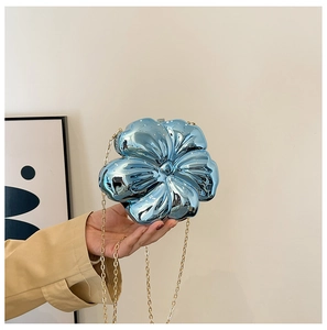 Detail of blue metallic flower clutch bag with golden chain strap held by model