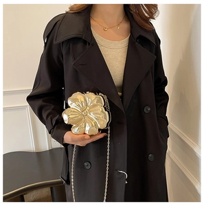 Detail of a golden flower-shaped acrylic evening bag with metallic petals and chain