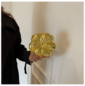 Detail of a golden flower-shaped hard shell evening bag with a metallic chain strap