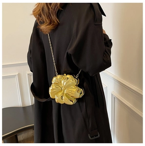 Detailed view of 3D gold flower clutch bag with metal chain strap on black coat