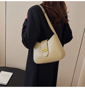 Chic beige underarm bag with gold metal buckle shown on a model in a minimalist style
